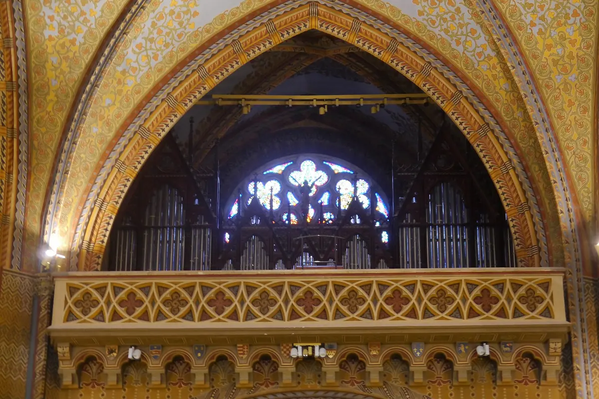 The organ loft of Matthias Church behind a carved gallery under a pointed arch, with a round stained-glass window above the pipes